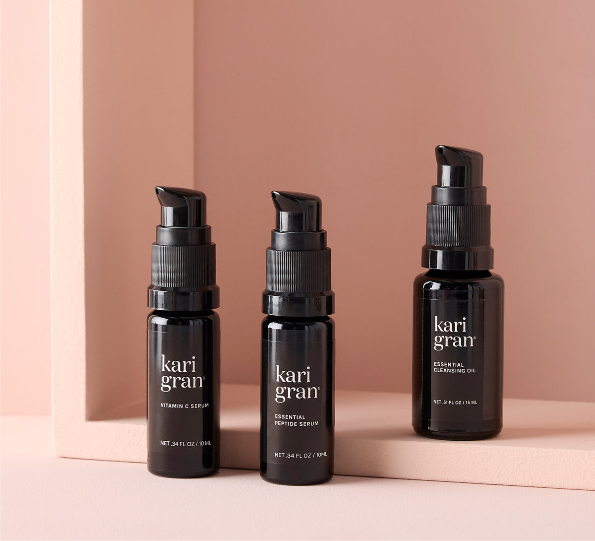 Three black bottles of kari gran skincare products on a peach background