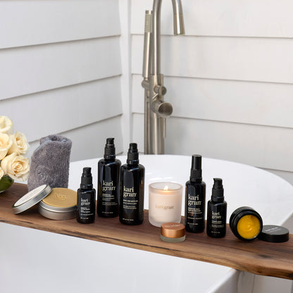 Bath products including bottles, a candle, and a towel on a wooden shelf with a bathtub in the background.