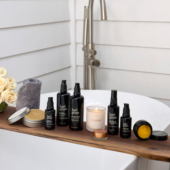 Bath products including bottles, a candle, and a towel on a wooden shelf with a bathtub in the background.
