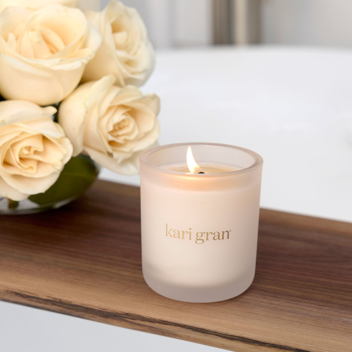 Frosted candle with 'kari gran' branding on a wooden surface next to cream roses.