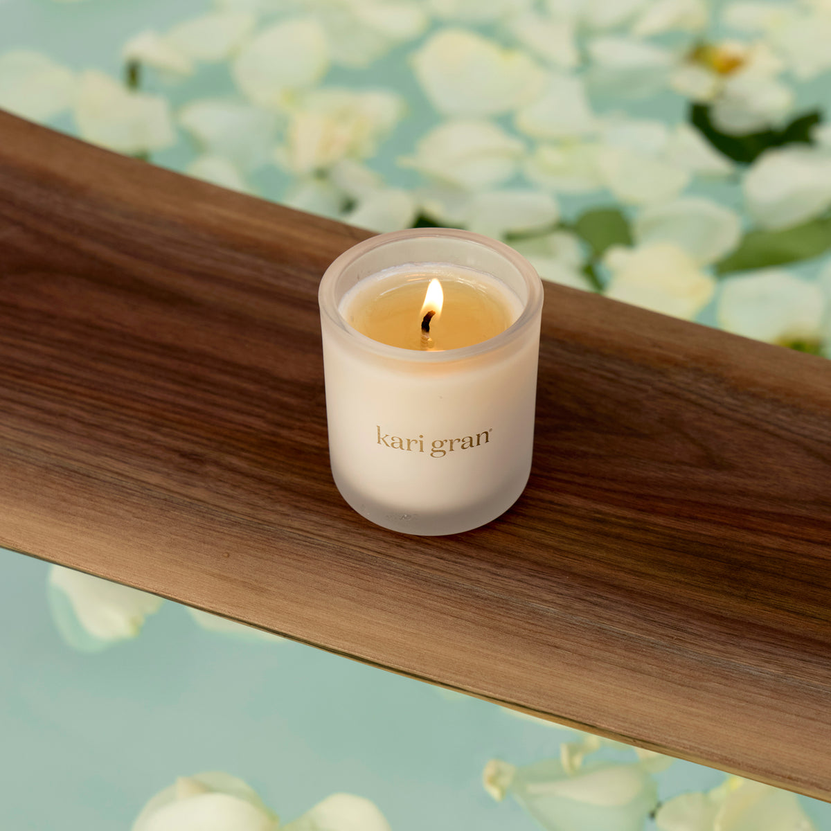 Lit candle in a 'kari gran' container on a wooden surface with a floral background