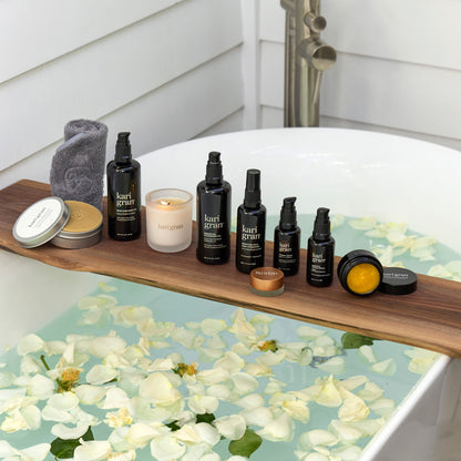 Bath products on a wooden shelf over a bathtub filled with water and flowers